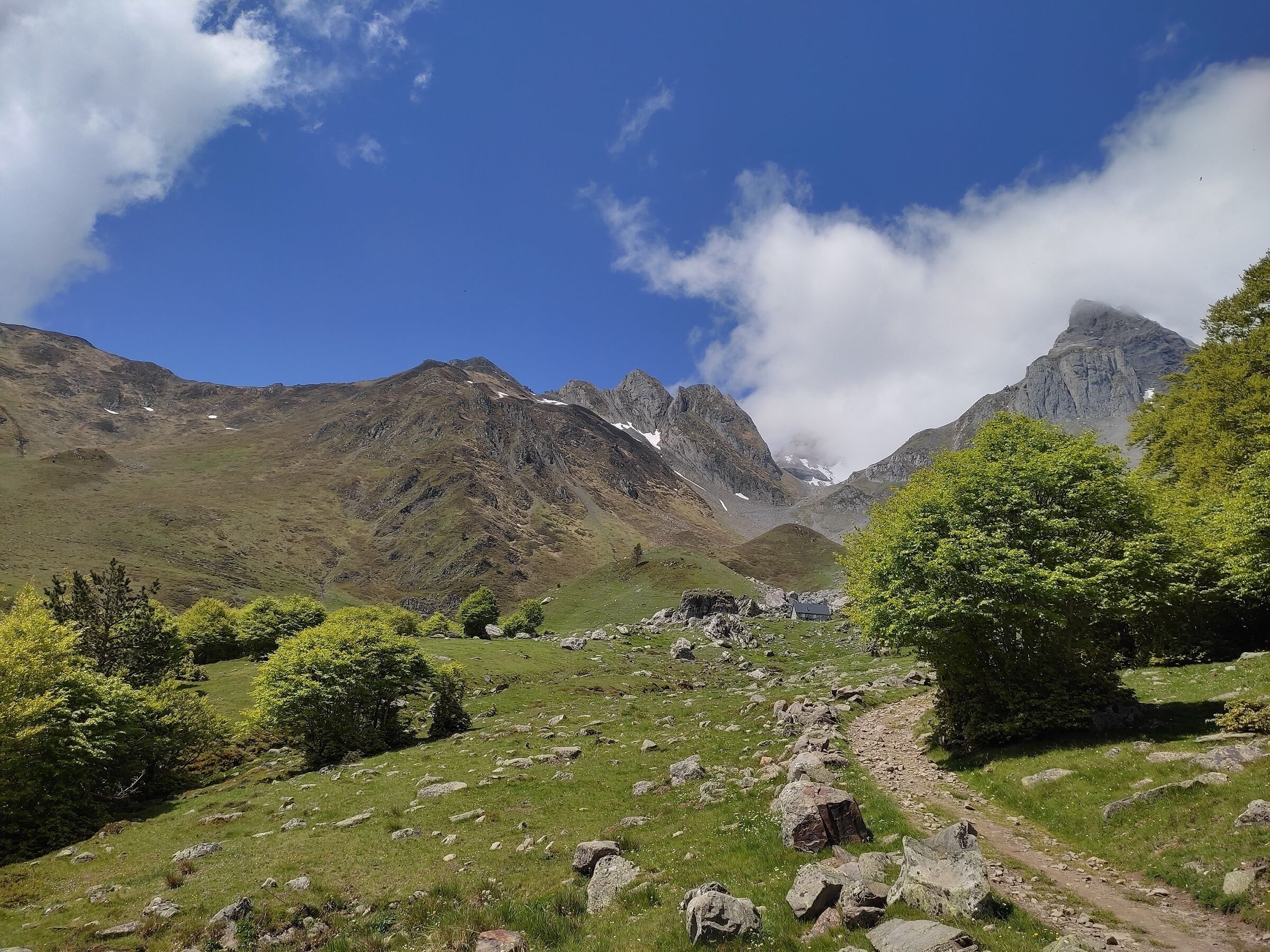 Un paisaje montañoso con cielo despejado, terreno rocoso y un camino que serpentea por el valle.