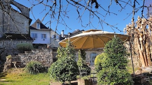 A stone wall with a wooden bench and two potted trees in a garden area.