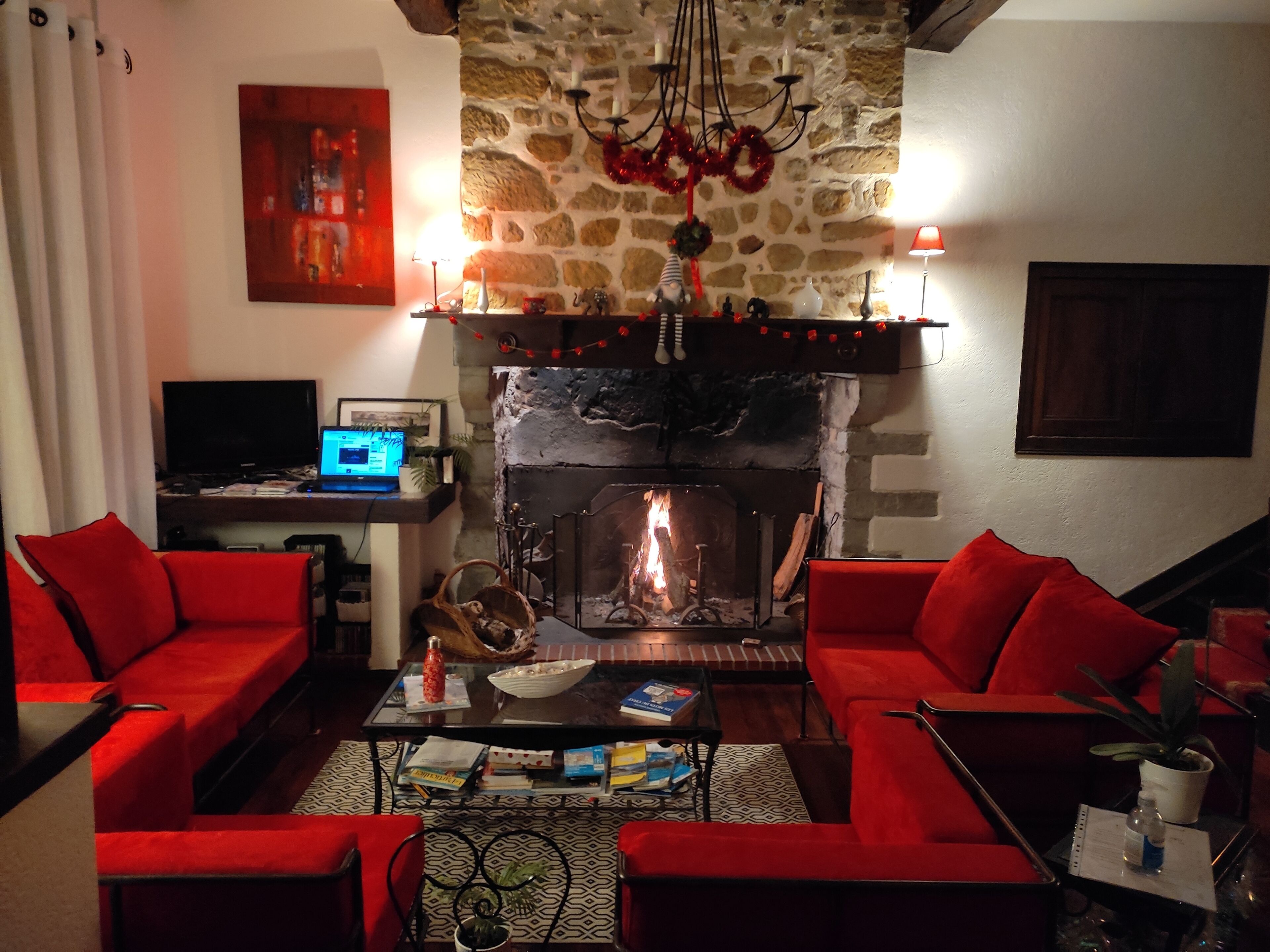 A cozy living room with red sofas, a fireplace, a laptop on a side table, and a stone wall.