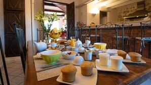 A breakfast table with various food items and drinks, a vase with flowers, and a kitchen area in the background.