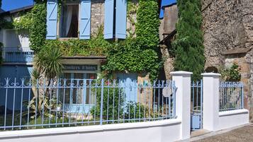 Un bâtiment en pierre avec des volets bleus et une enseigne indiquant « Chambres d’hôtes ».