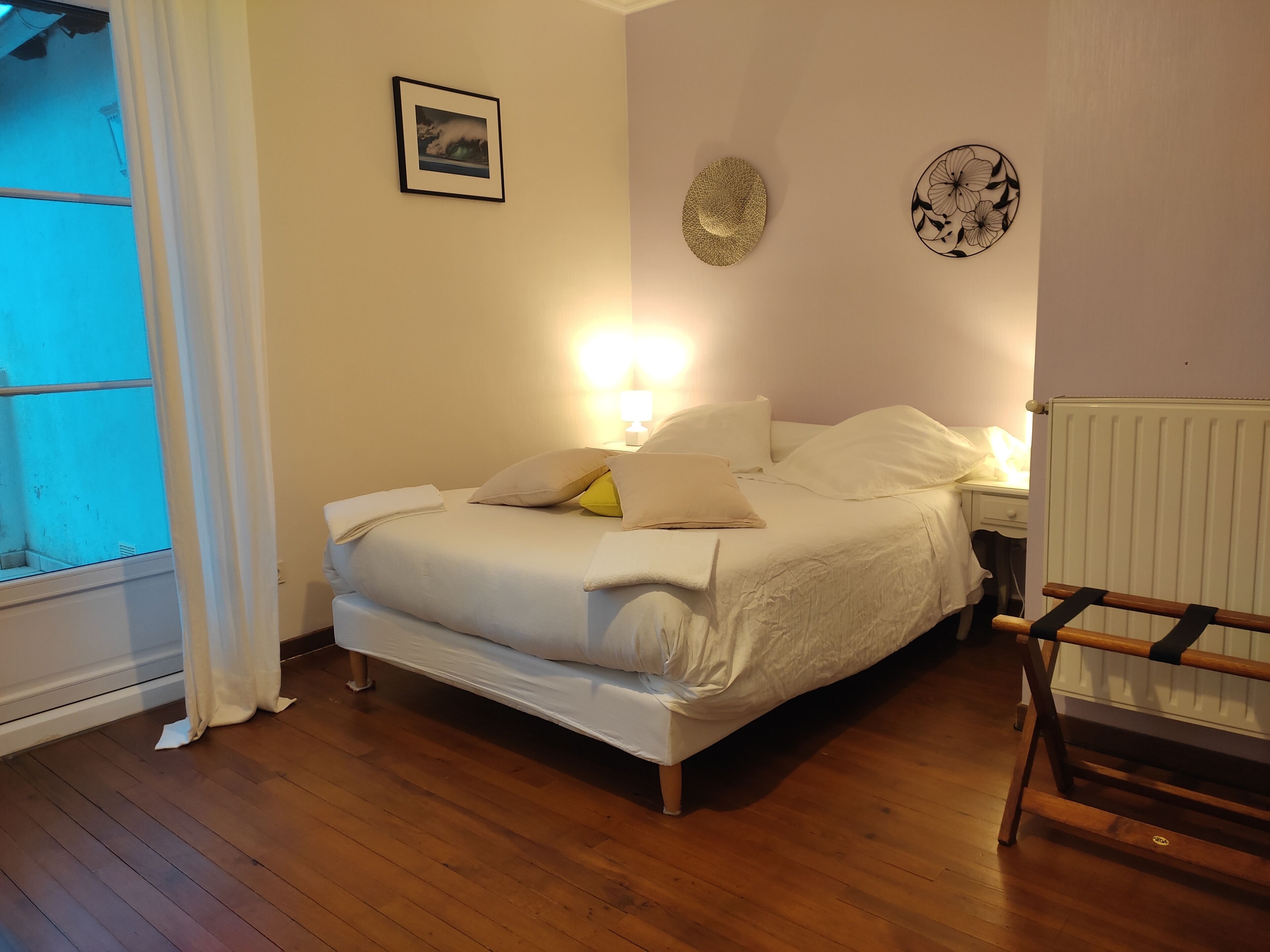 Un dormitorio con cama, mesitas de noche, un radiador y una ventana con cortinas.