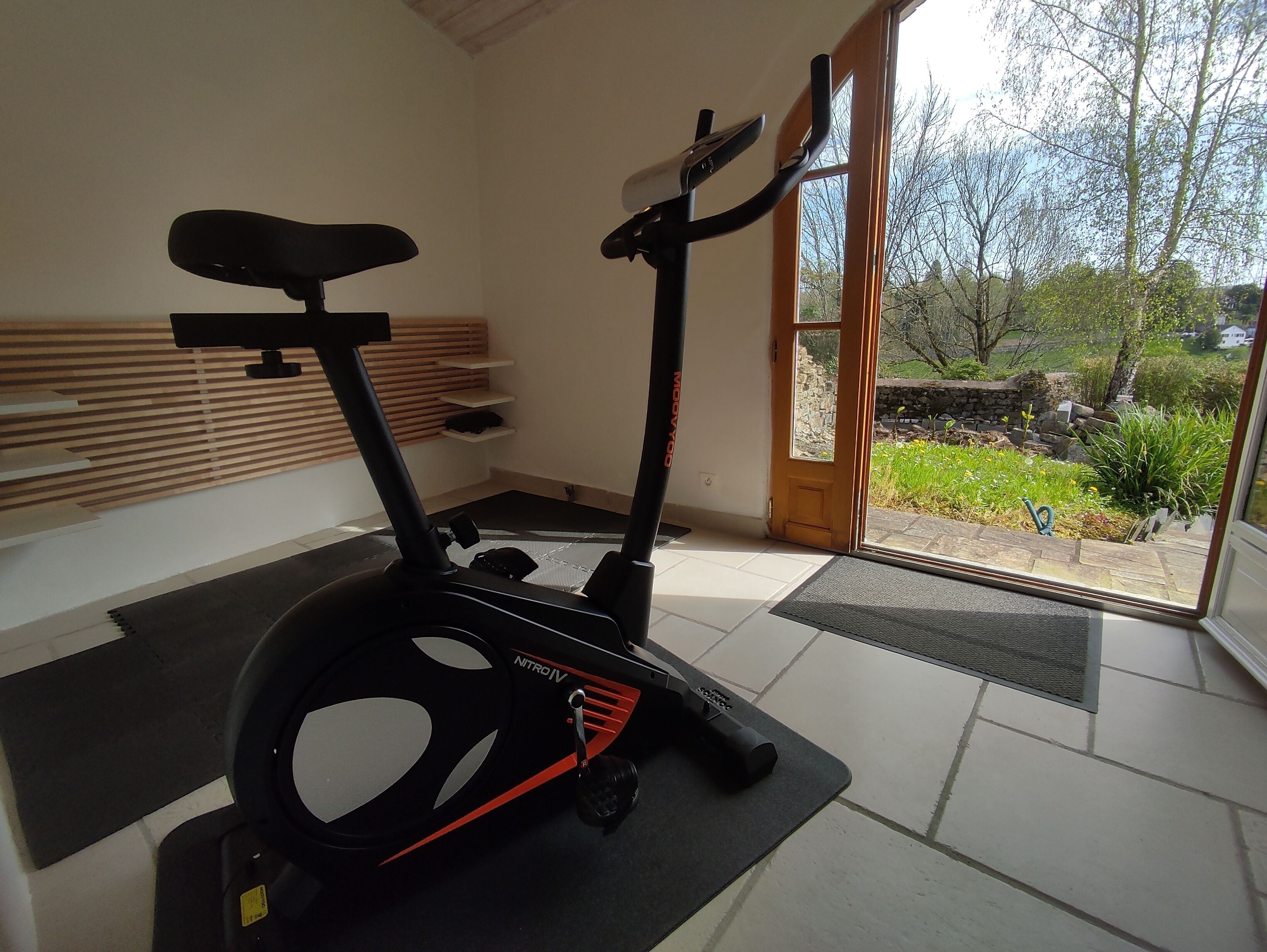 Een overdekte hometrainer in een kamer met uitzicht op een tuin door een glazen deur.