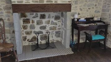 Habitación con pared de piedra, chimenea, una silla de madera, un escritorio con lámpara y una alfombra estampada.
