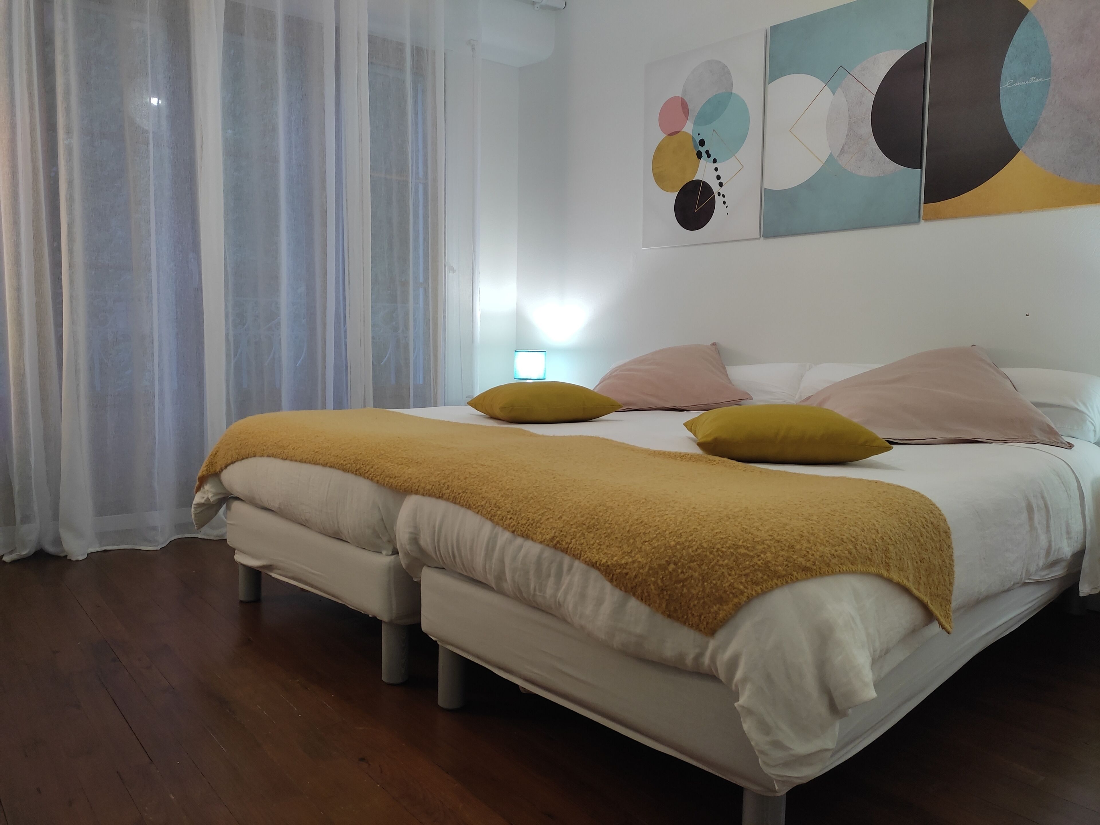 A double bed with a mustard-colored blanket, two pillows, and a bedside table with a lamp.