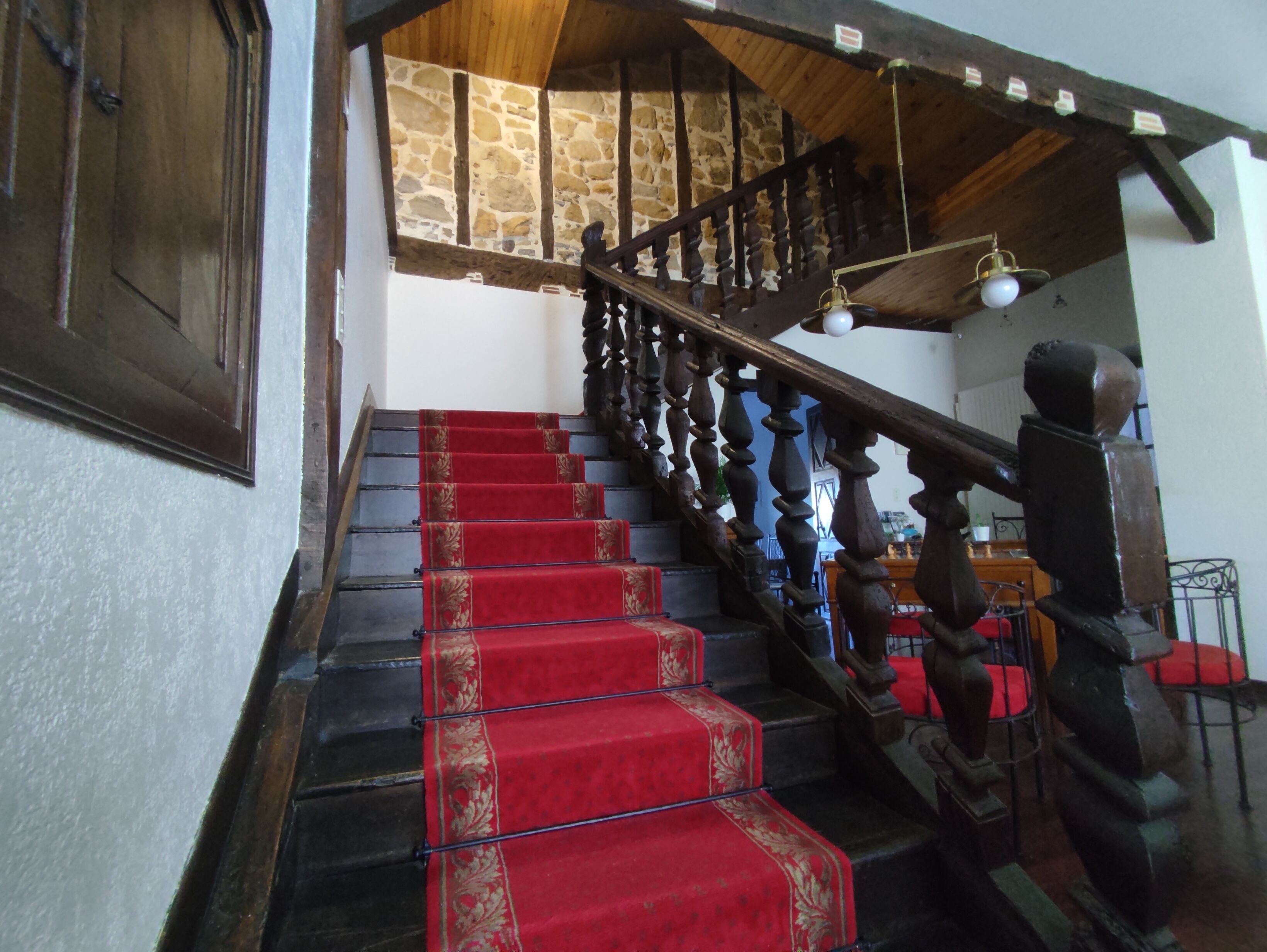 Una escalera con peldaños cubiertos de alfombra roja, barandillas de madera y un muro de piedra.