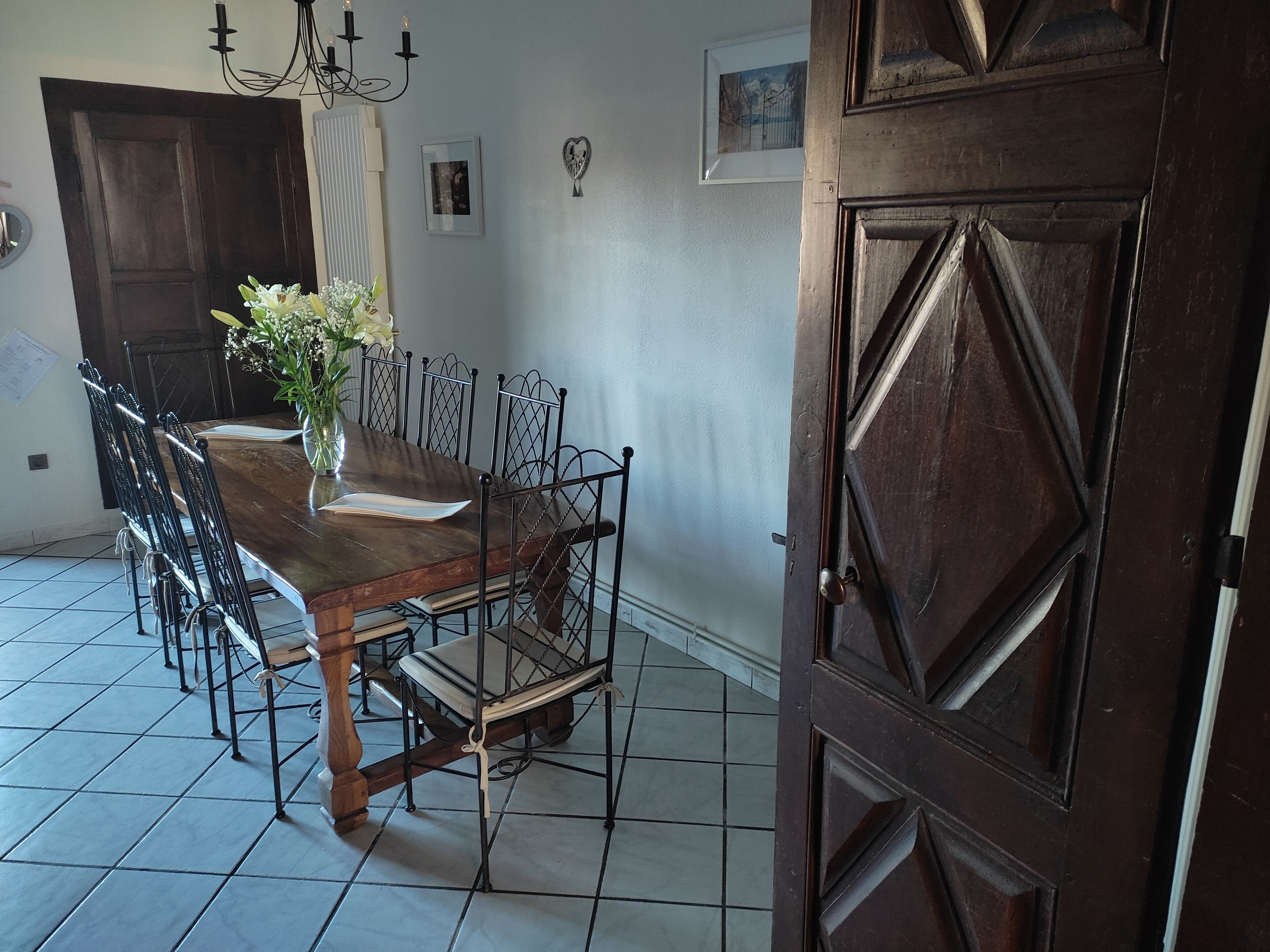 A dining area with a wooden table, metal chairs, a vase with flowers, a chandelier, and a wooden door.