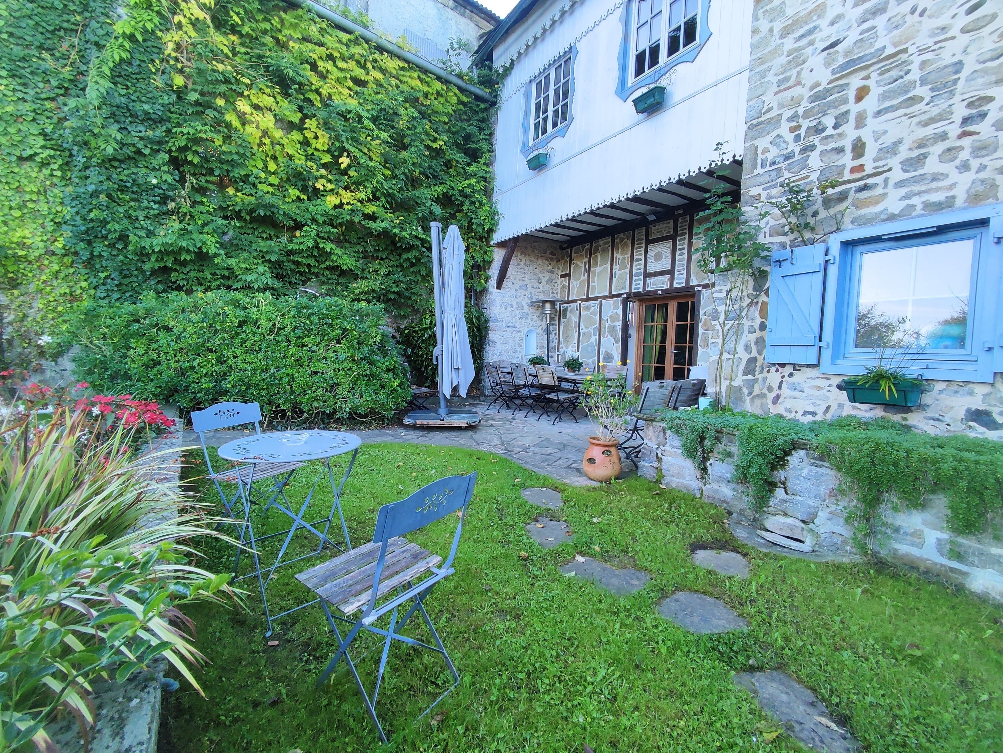 Un bâtiment en pierre doté d’un patio couvert, d’un espace extérieur aménagé pour s’asseoir et d’un jardin avec un petit étang.