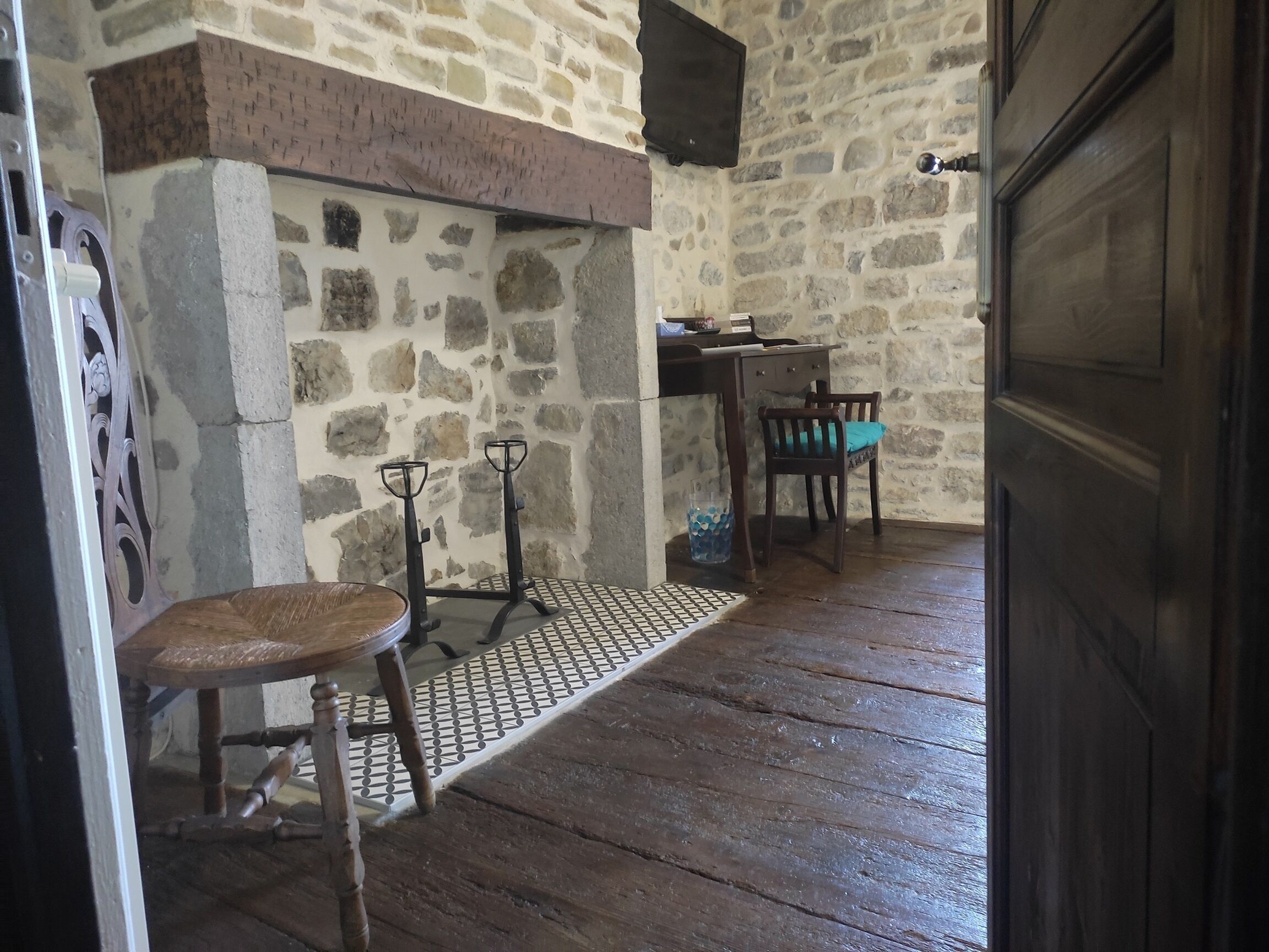 Una habitación rústica con paredes de piedra, suelo de madera, una mesa con sillas y una puerta.
