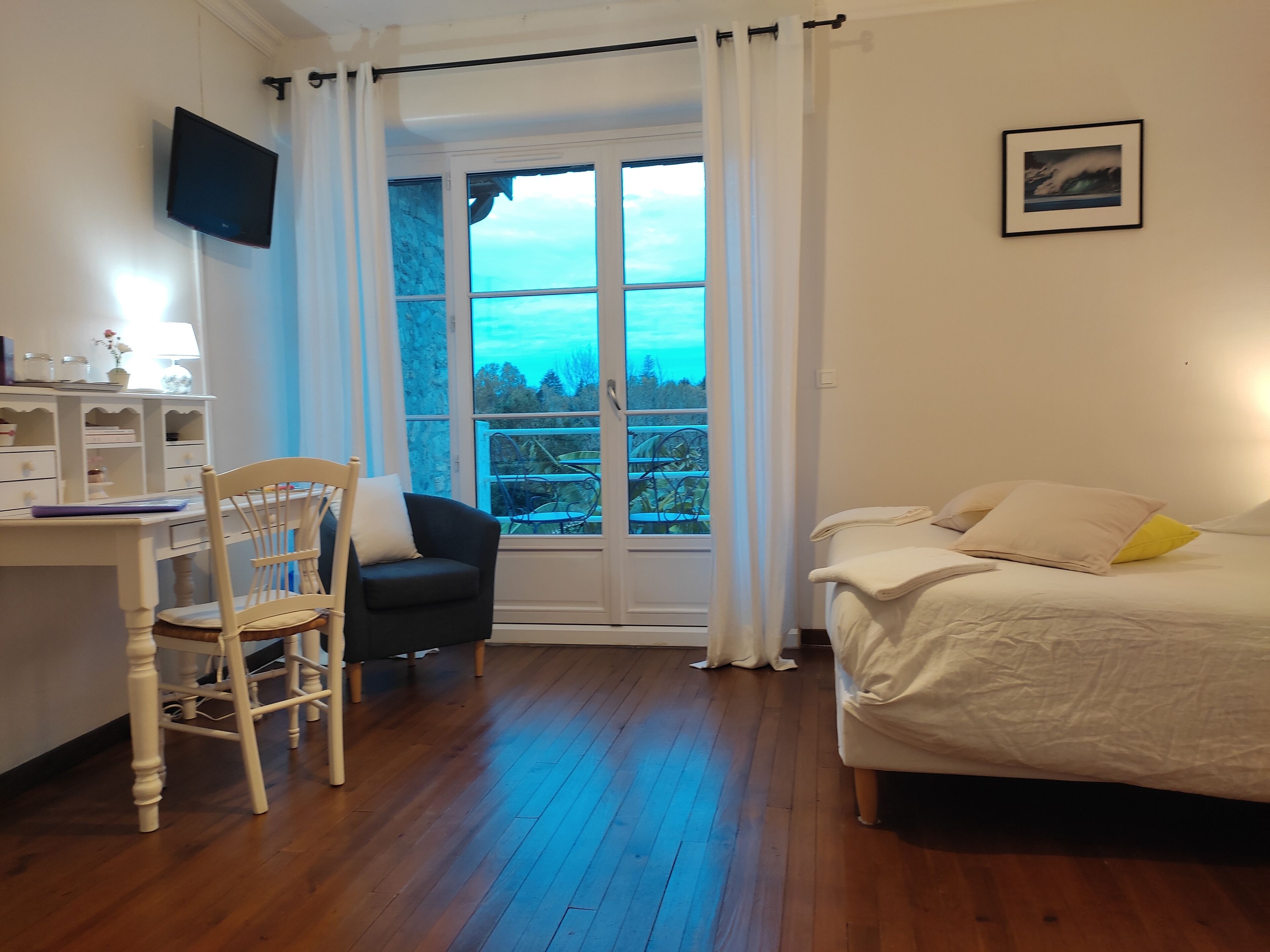 A bedroom with a bed, a desk with a chair, a TV on the wall, and a window with curtains.