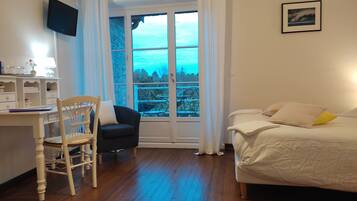 A bedroom with a bed, a desk with a chair, a TV on the wall, and a window with curtains.