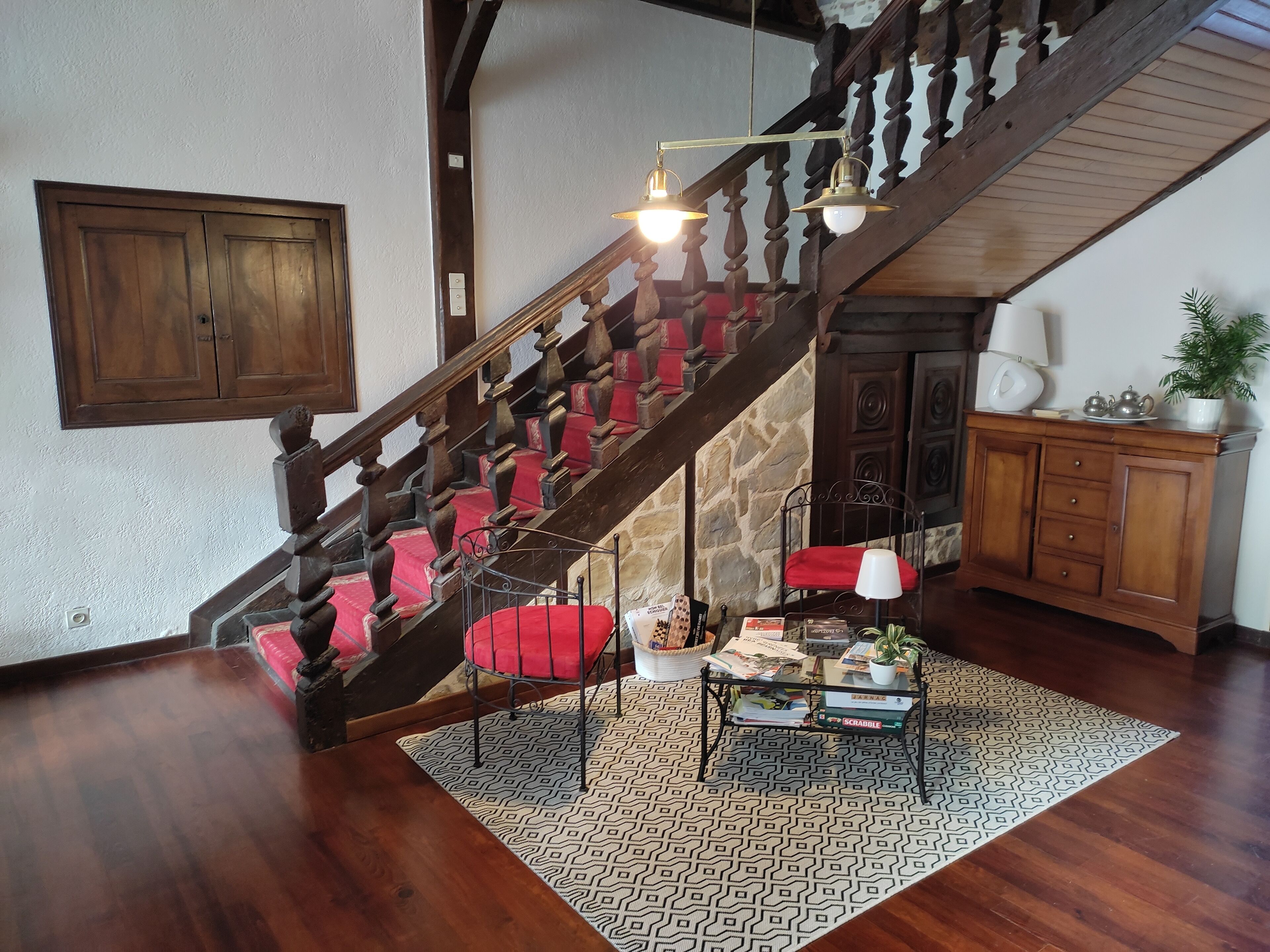 A wooden staircase with red cushioned steps, a patterned rug, and a metal table with magazines and a lamp.