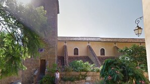 A courtyard with a stone pathway, a person standing, and a building with a tiled roof. - 3-room apartment with pool and garage, near the beach (Bormes-les-Mimosas)