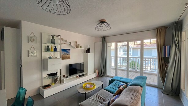 Een moderne woonkamer met een televisie, bank en stoelen. Decoratieve objecten staan op planken en er is een balkon met uitzicht.
