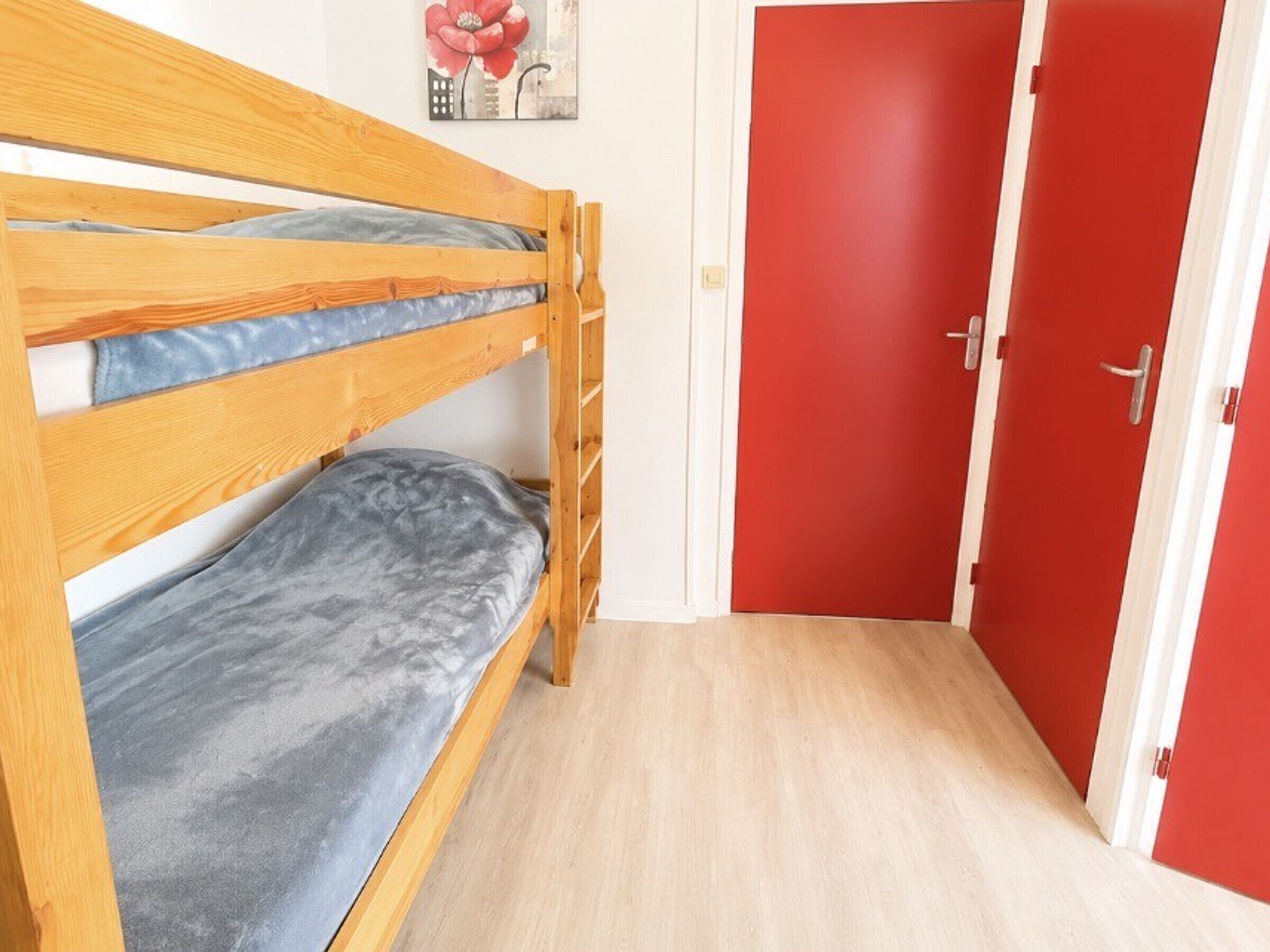 A bunk bed with grey bedding, a red door, and a light wooden floor.