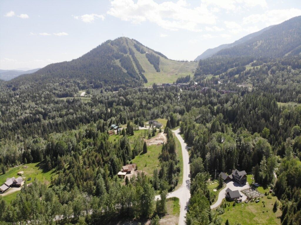 A rural landscape with a winding road, scattered houses, and dense forested hills.