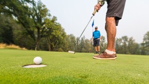 Una pallina da golf su un tee, su un campo verde con un bastoncino segnalino sullo sfondo.