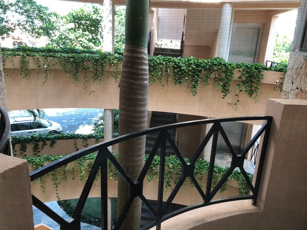 Een balkon met een metalen hek, omringd door groen en een uitzicht op een auto en gebouwen.