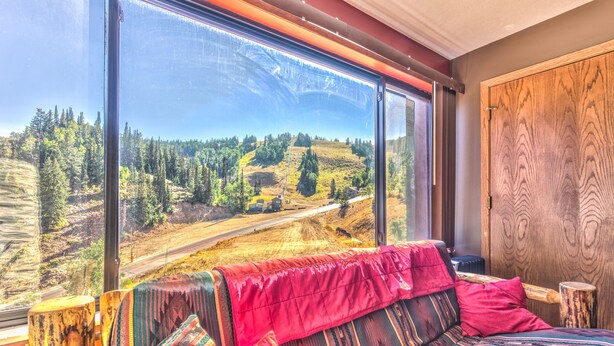 Ein Zimmer mit großem Fenster und Blick auf eine bewaldete Landschaft sowie eine Straße.