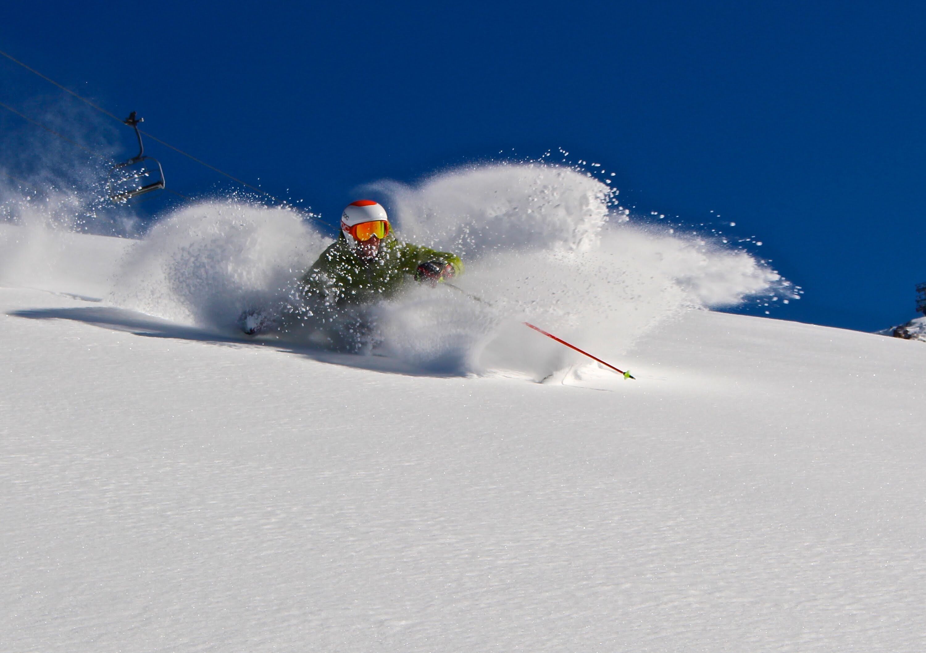 Un skieur en mouvement, entouré de neige, avec un ciel bleu dégagé en arrière-plan.