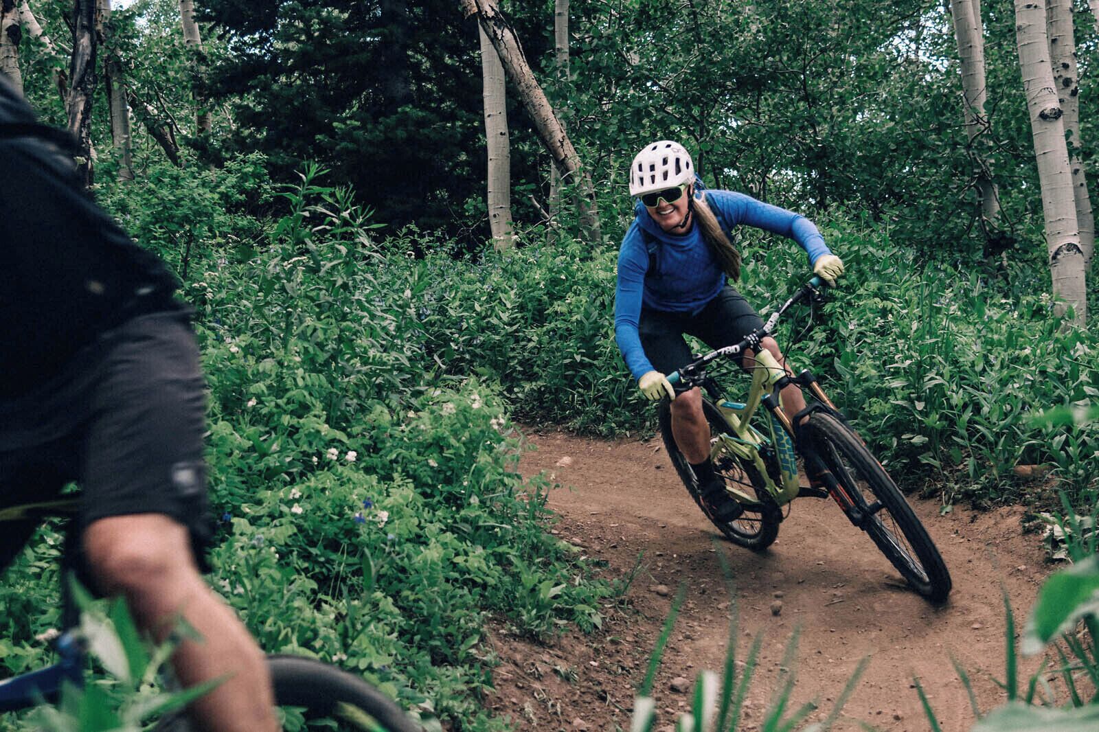 Eine Person fährt ein Mountainbike auf einem unbefestigten Weg, umgeben von viel Grün.