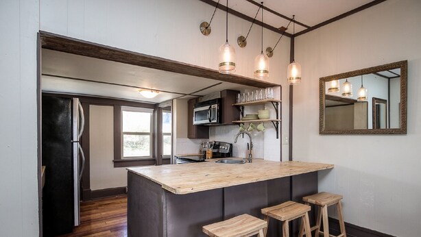 A kitchen with a central island, wooden stools, a refrigerator, a microwave, and hanging pendant lights. - Cottage On Main- In The Heart Of Weston (Weston)