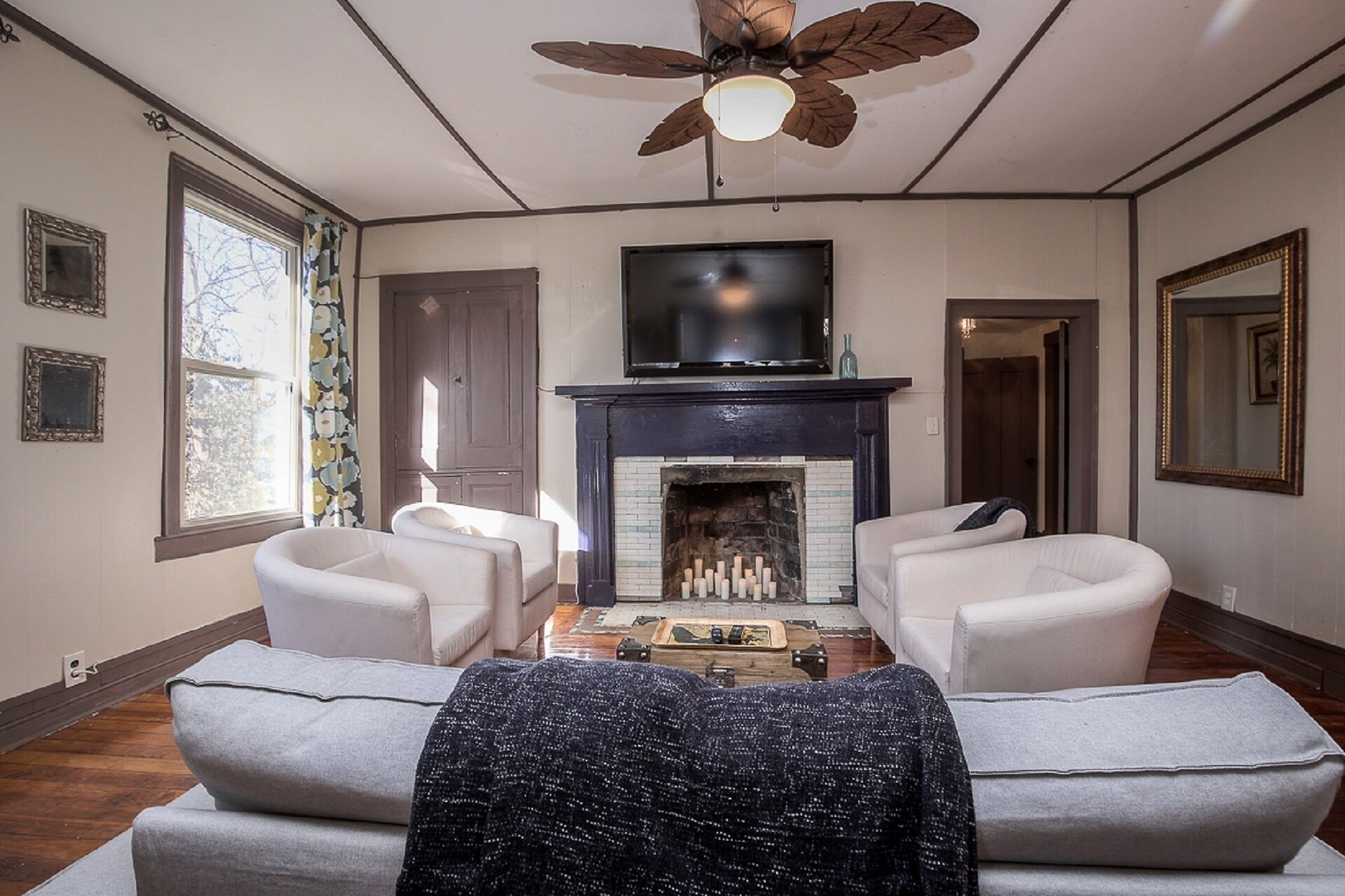 A living room with a fireplace, two sofas, a ceiling fan, and a TV mounted above the fireplace.