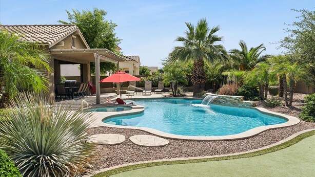 Ein Pool mit Wasserfall, umgeben von Palmen und einer überdachten Terrasse.