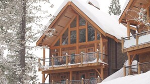 A wooden chalet with a balcony and large windows, surrounded by snow. - Ski In, Ski Out Awesomeness! (Rossland)