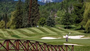 A golf course with a wooden bridge, a golfer, and a mountainous backdrop. - Ski In, Ski Out Awesomeness! (Rossland)
