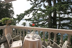Un balcon avec une table dressée pour le thé, donnant sur un lac et entouré d’arbres.
