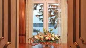 Une salle à manger élégante, avec une table en bois, des chaises décorées et une grande fenêtre offrant une vue pittoresque sur les arbres et un lac.