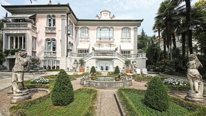 Un grand bâtiment historique doté d’un jardin à la française, comprenant des statues et une fontaine.