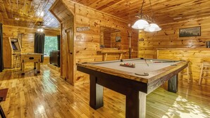 A wooden cabin interior with a pool table, a foosball table, and a bar area. - Private Wooded Setting! Theater Room! Centrally Located! 3 Decks! Fun Game Room  (Sevierville)