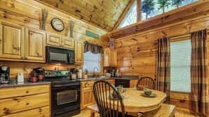 A wooden cabin kitchen with a dining table, chairs, a clock, and a 'Welcome to the Mountain' sign. - Private Wooded Setting! Theater Room! Centrally Located! 3 Decks! Fun Game Room  (Sevierville)