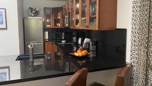 Moderni keittiö, jossa on mustat työtasot, puukaapit ja keskellä sijaitseva saareke, jonka päällä on hedelmiä.