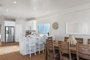 Una cocina moderna con armarios blancos, un refrigerador de acero inoxidable y un comedor con sillas de madera y una mesa blanca.