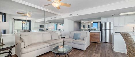 Un salon moderne avec une table basse en verre, un canapé beige et un ventilateur de plafond.