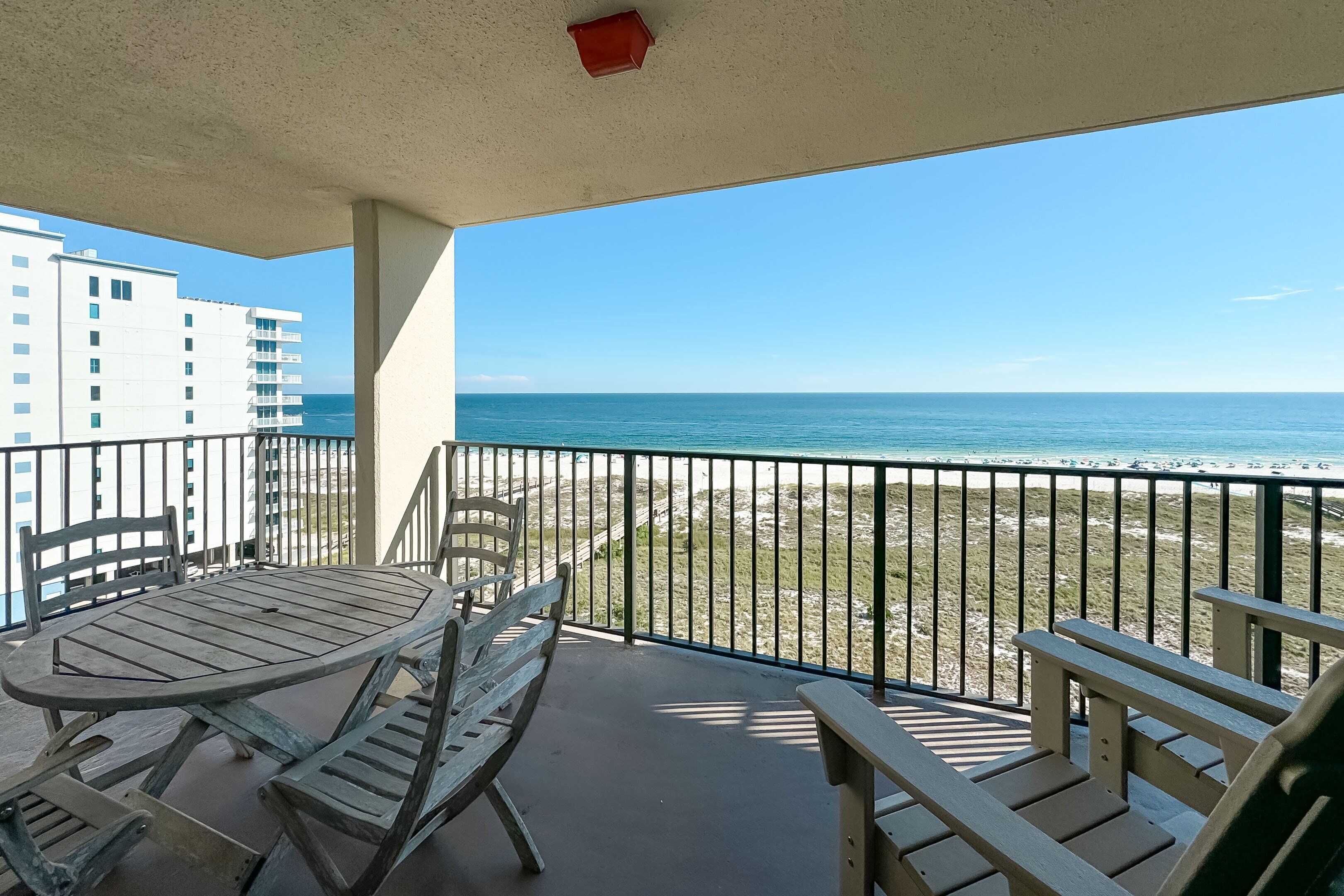 Un balcon avec une table et des chaises en bois, donnant sur une plage et l’océan.