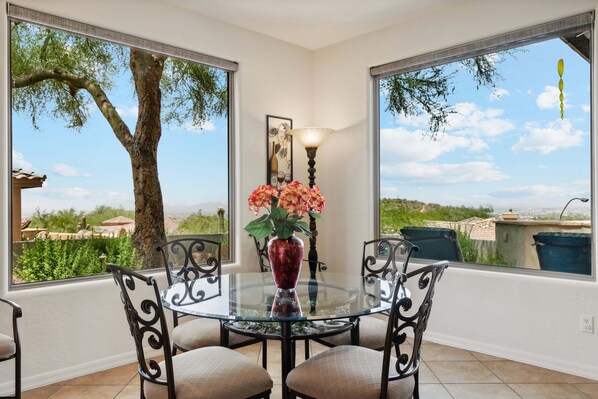 A glass table with four chairs, a vase with flowers, and a lamp.