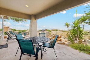 An outdoor patio with a round table and chairs, a covered area with a view of the landscape, and a stone pathway.