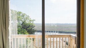 Een kamer met een schuifglazen deur die leidt naar een balkon met uitzicht op een landschap en een waterpartij.