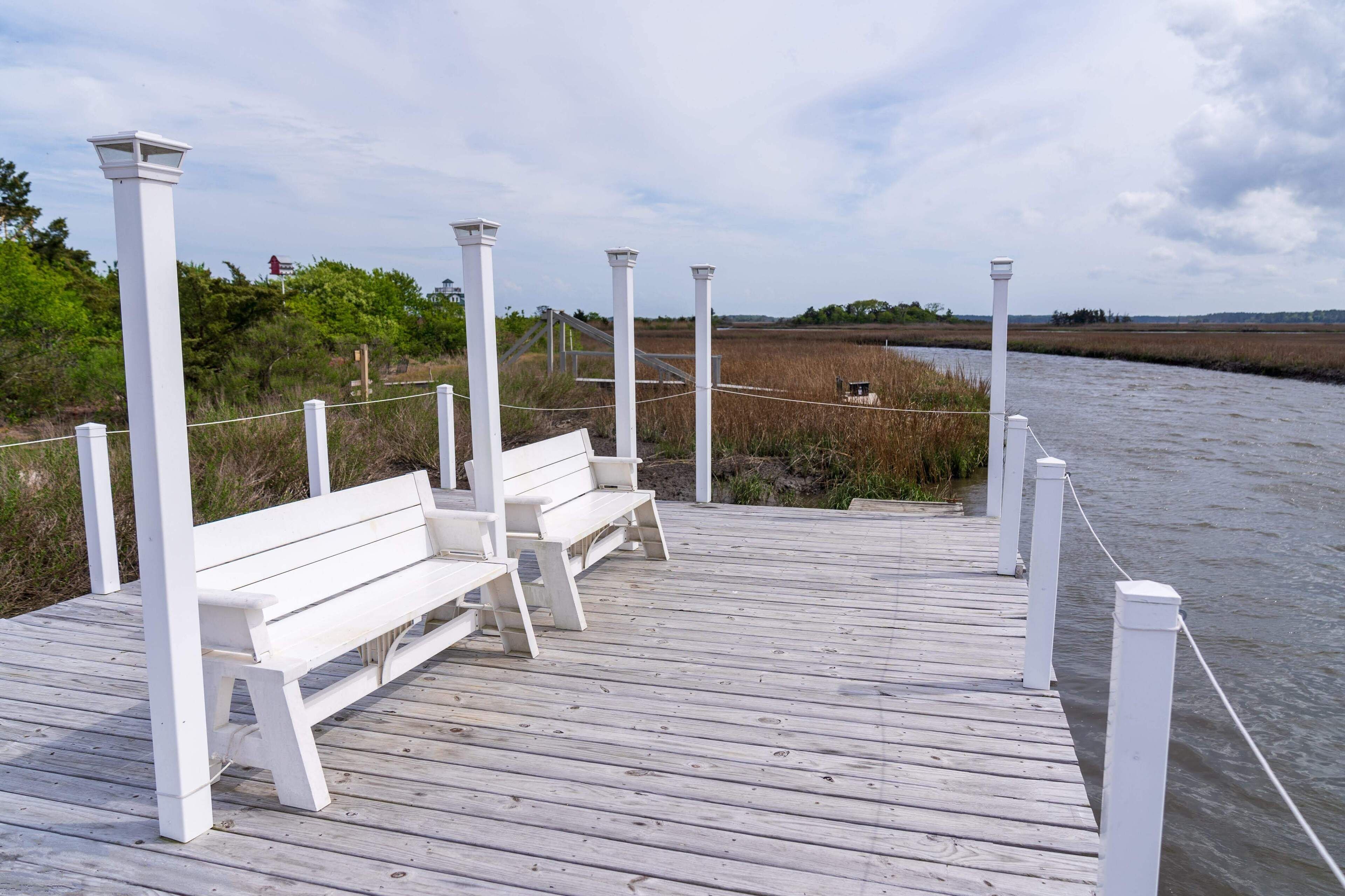 A wooden pier with white railings and benches, leading to a body of water.