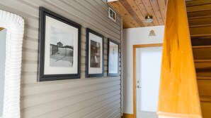 Een gang met ingelijste foto's aan de muur, een houten leuning en een deur aan het einde.