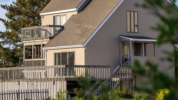 Een huis met twee verdiepingen, een balkon, een houten hek en een vijver op de voorgrond.
