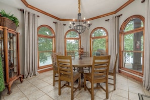 Enjoy meals in this dining area with a round table and six chairs, surrounded by large windows and a chandelier.
