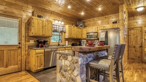 A wooden cabin-style kitchen with stone accents, wooden cabinets, a stone island, and a stainless steel refrigerator. - Amazing Luxury Log Cabin! Great Living Space! Mountain Views! 2 Jacuzzi Tubs!  (Sevierville)