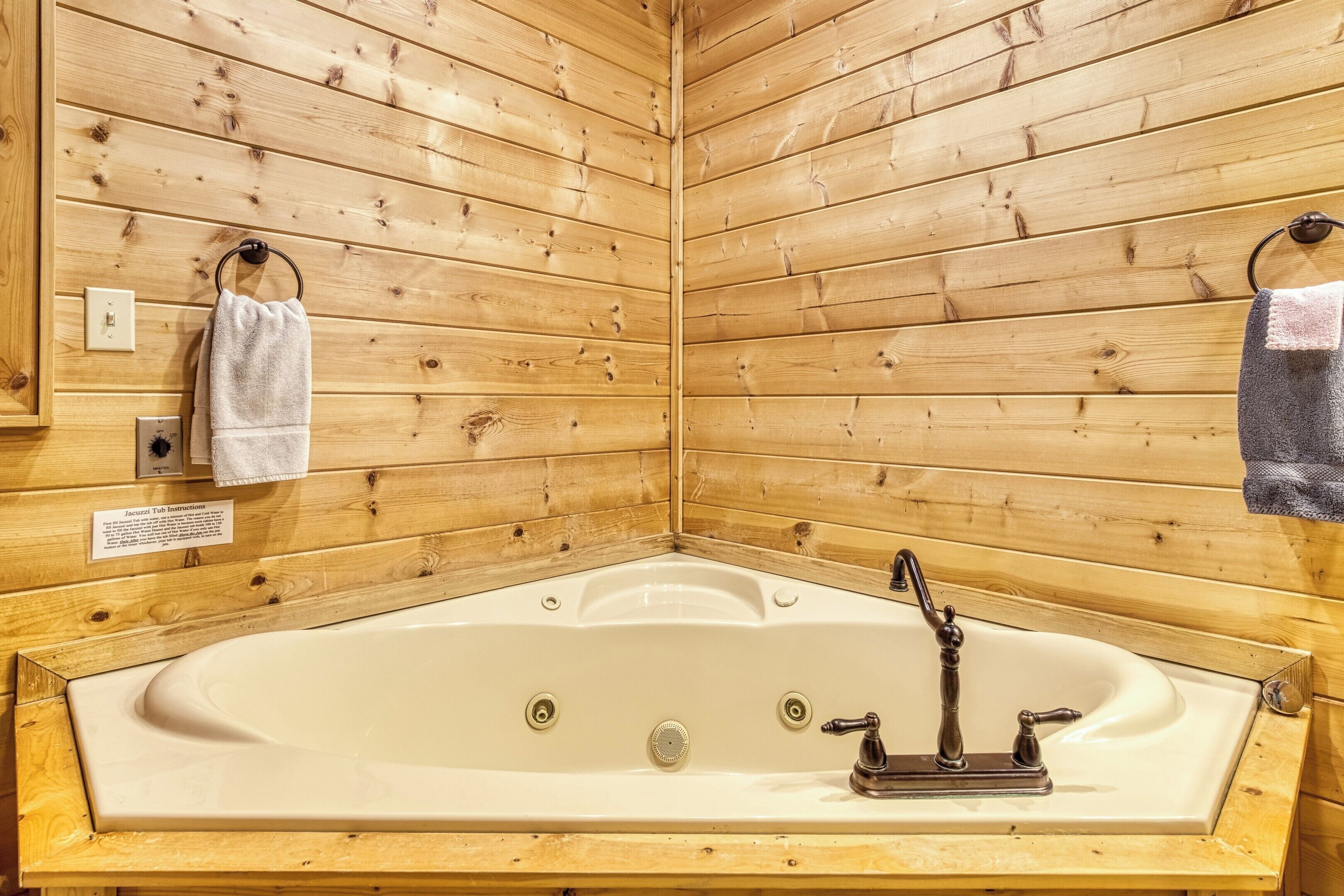 A wooden cabin with a large bathtub, wooden walls, and two towels hanging on hooks.