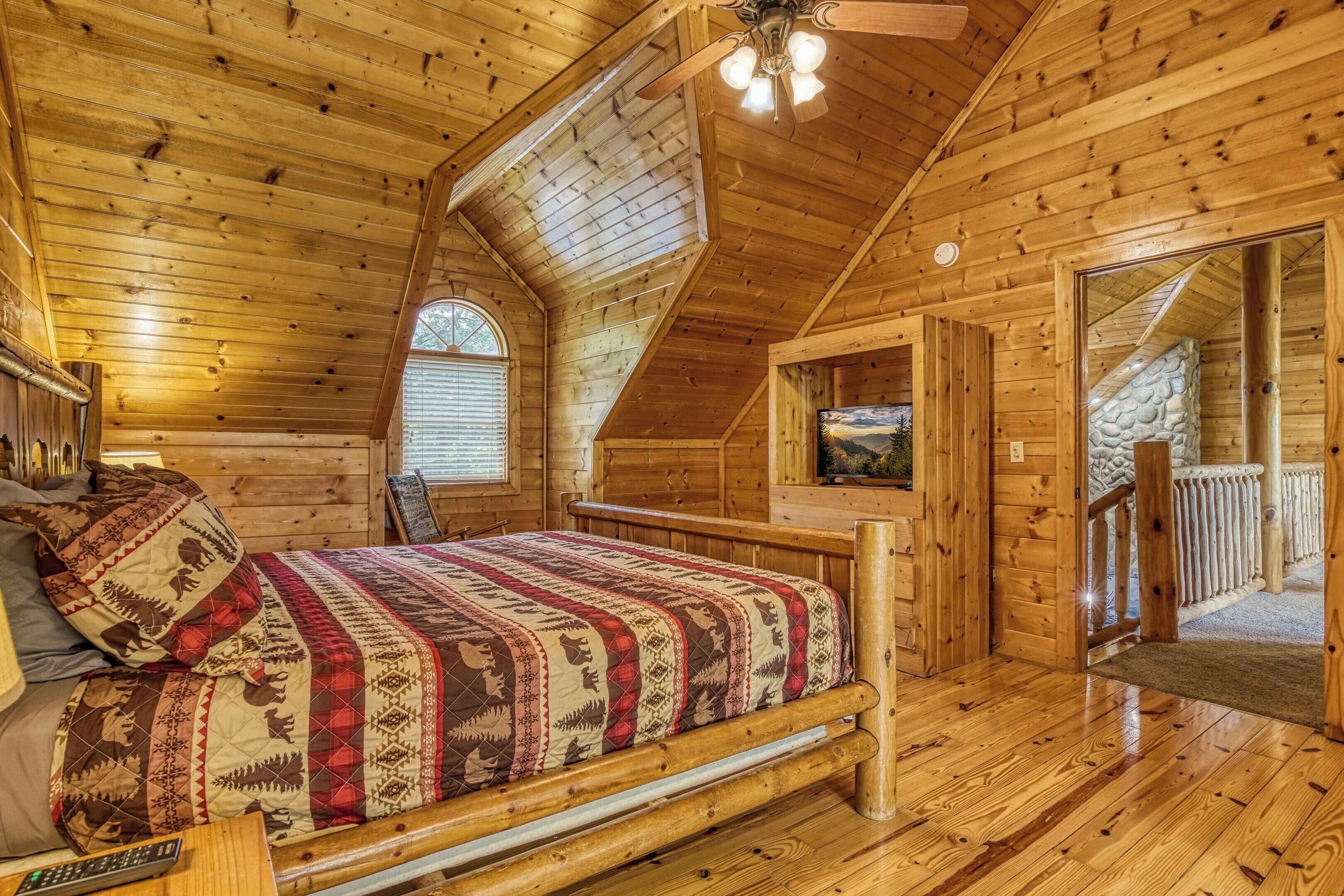 Une chambre dans une cabane en bois, avec un lit, un ventilateur de plafond et une cheminée en pierre.
