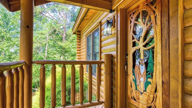 A wooden cabin with a porch, a carved door, and a window. - Amazing Luxury Log Cabin! Great Living Space! Mountain Views! 2 Jacuzzi Tubs!  (Sevierville)